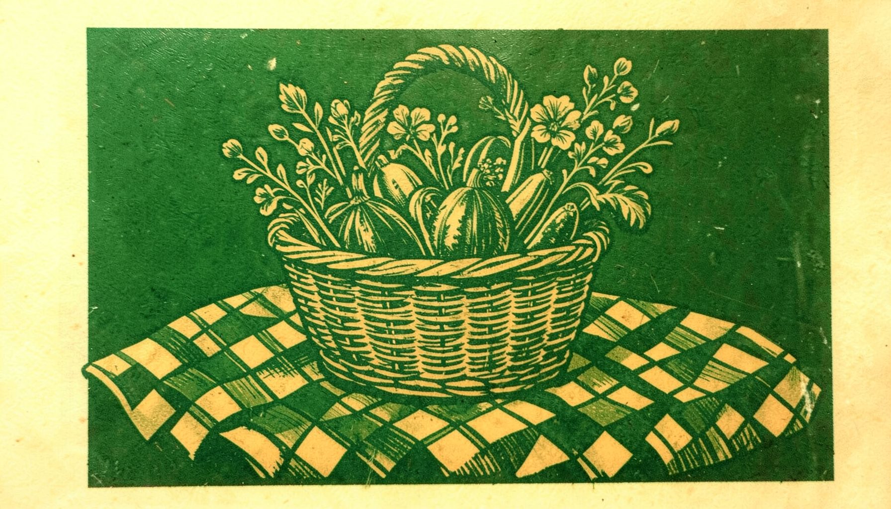 Gravure sur linoléum représentant un panier en osier rempli de légumes et de fleurs, posé sur une nappe à carreaux, dans des tons verts profonds et ocres chaleureux